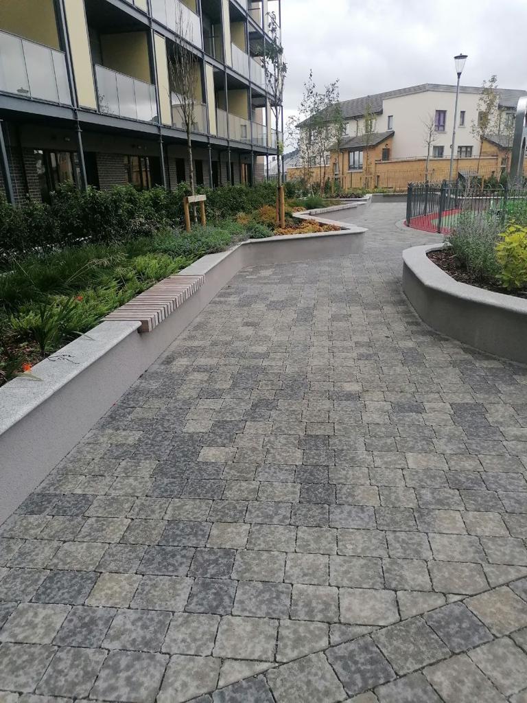 A paved walkway with a flower bed and a modern apartment building